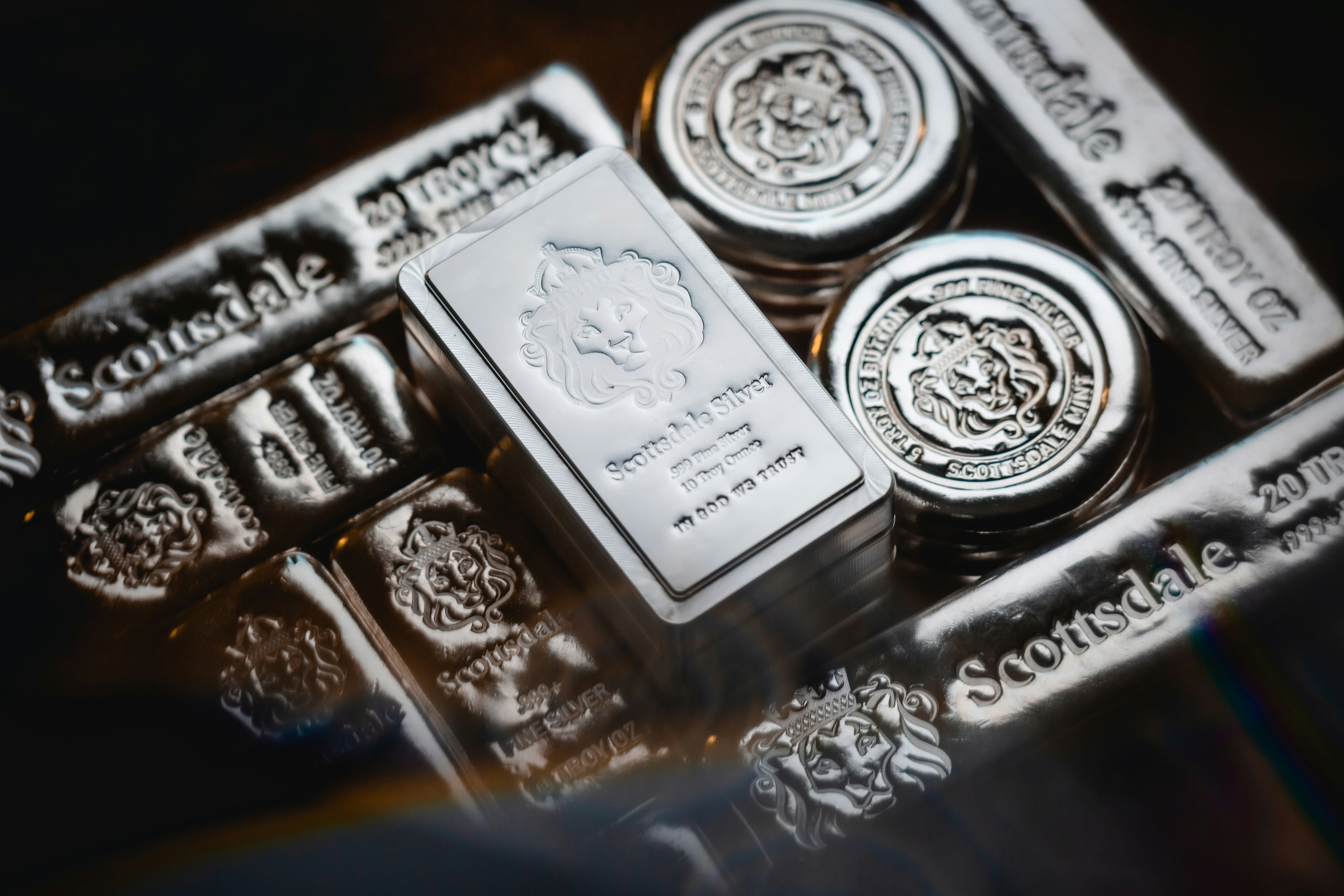 Silver bars stacked alongside individual coins arranged on a dark background.