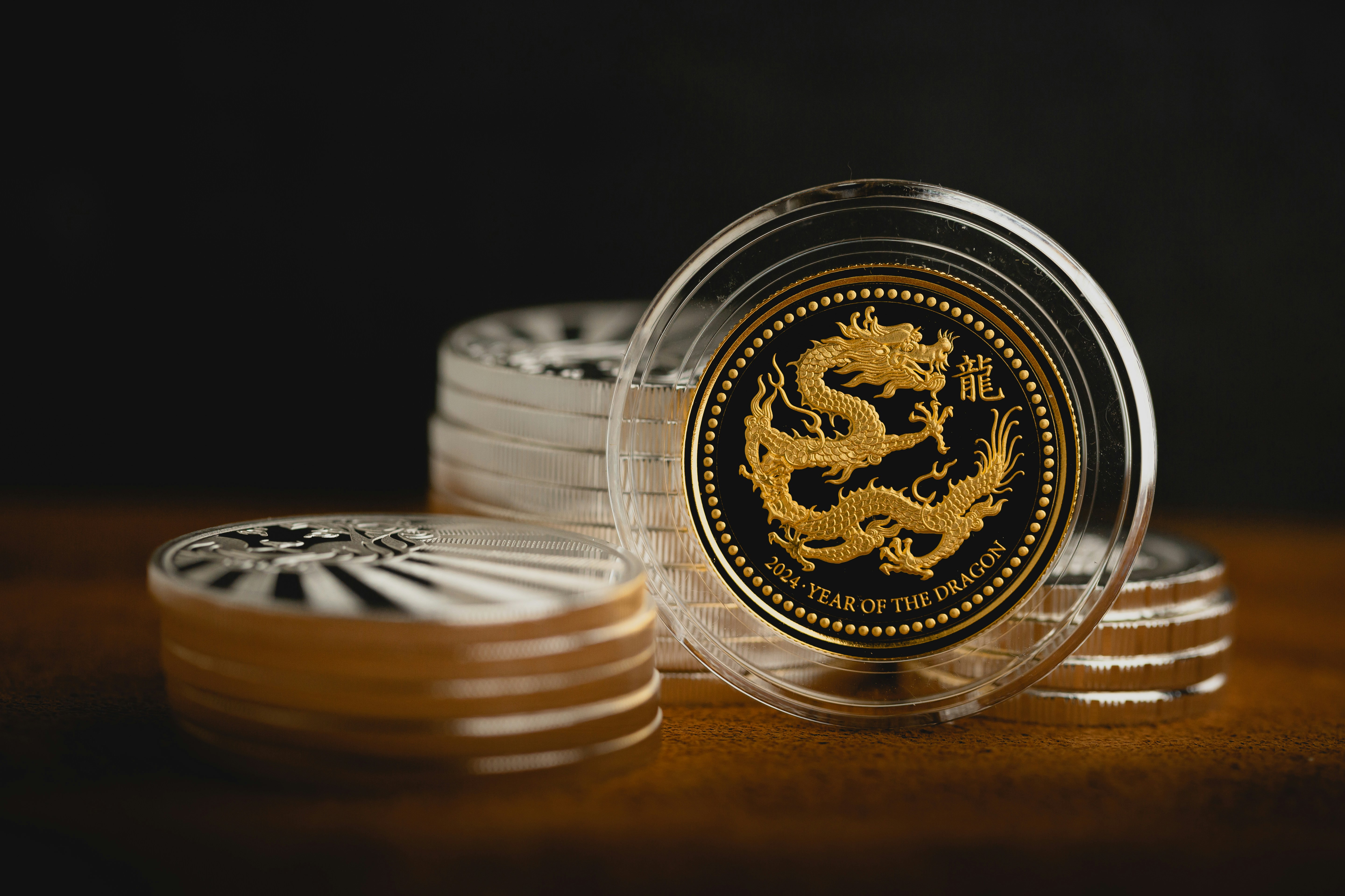 Gold and silver coins in protective cases arranged on a warm surface with professional lighting.