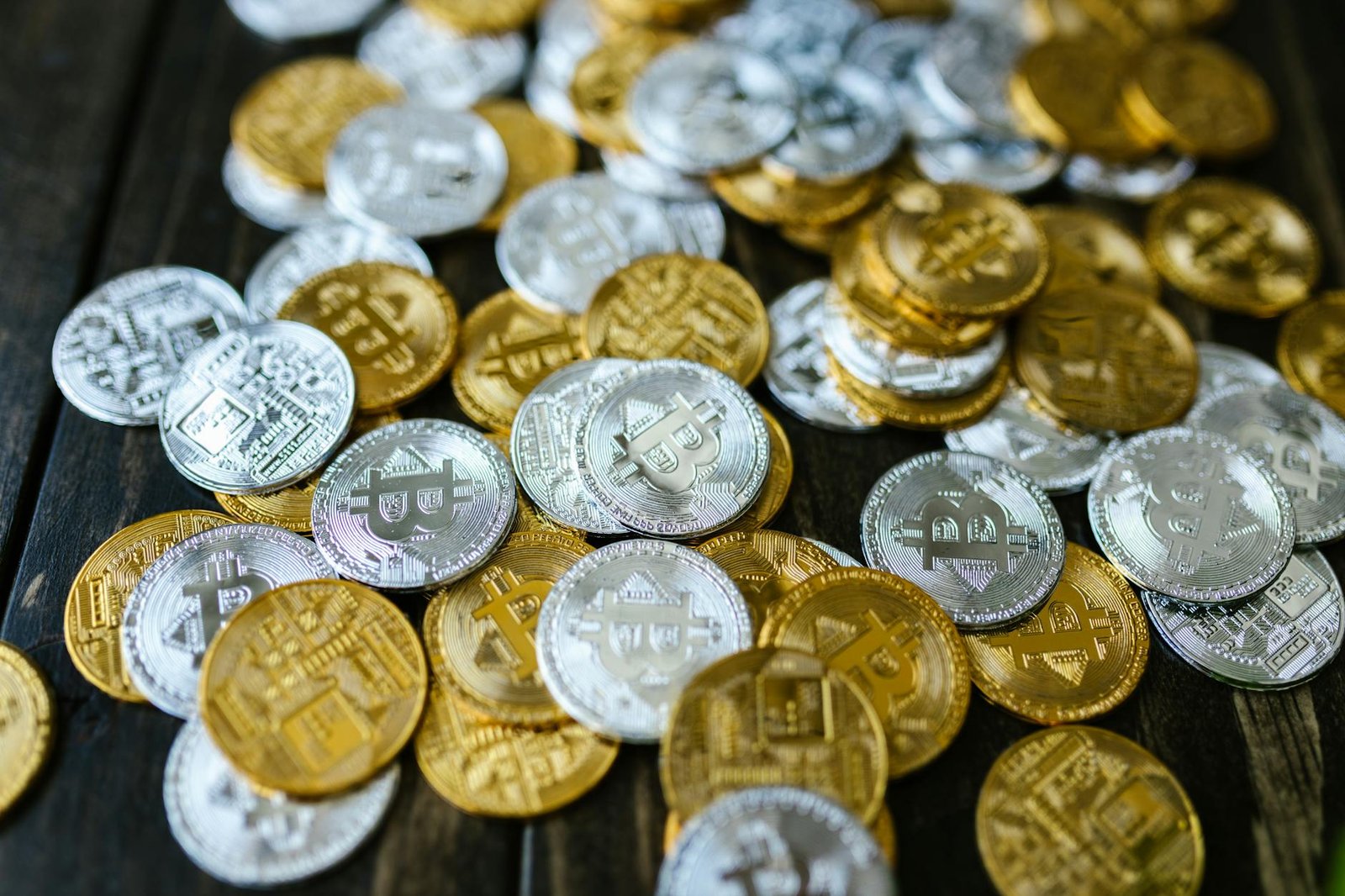A detailed view of scattered gold and silver Bitcoin coins on a wooden table.