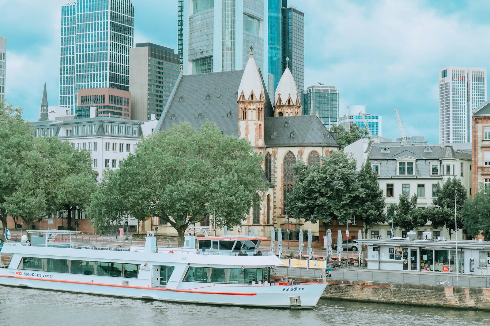 Frankfurt cityscape featuring a historic church, modern skyscrapers, and a boat along the river.