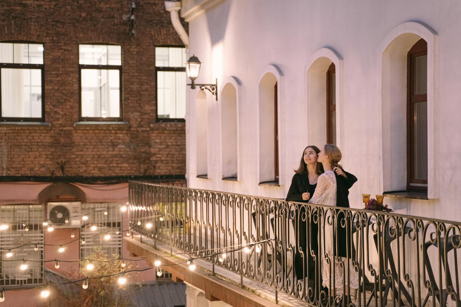 A couple enjoys a romantic evening together on a charming urban balcony under string lights.