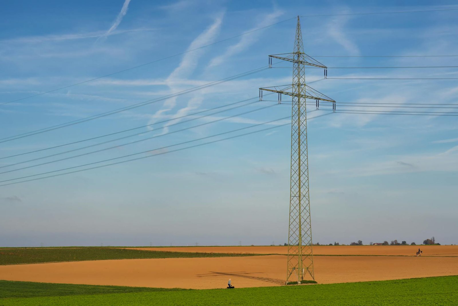 High voltage power line standing tall in a vast agricultural field under a clear blue sky in Germany.