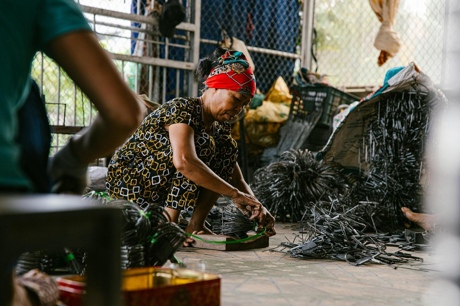 Focused woman working in a recycling center sorting metal parts on the floor.