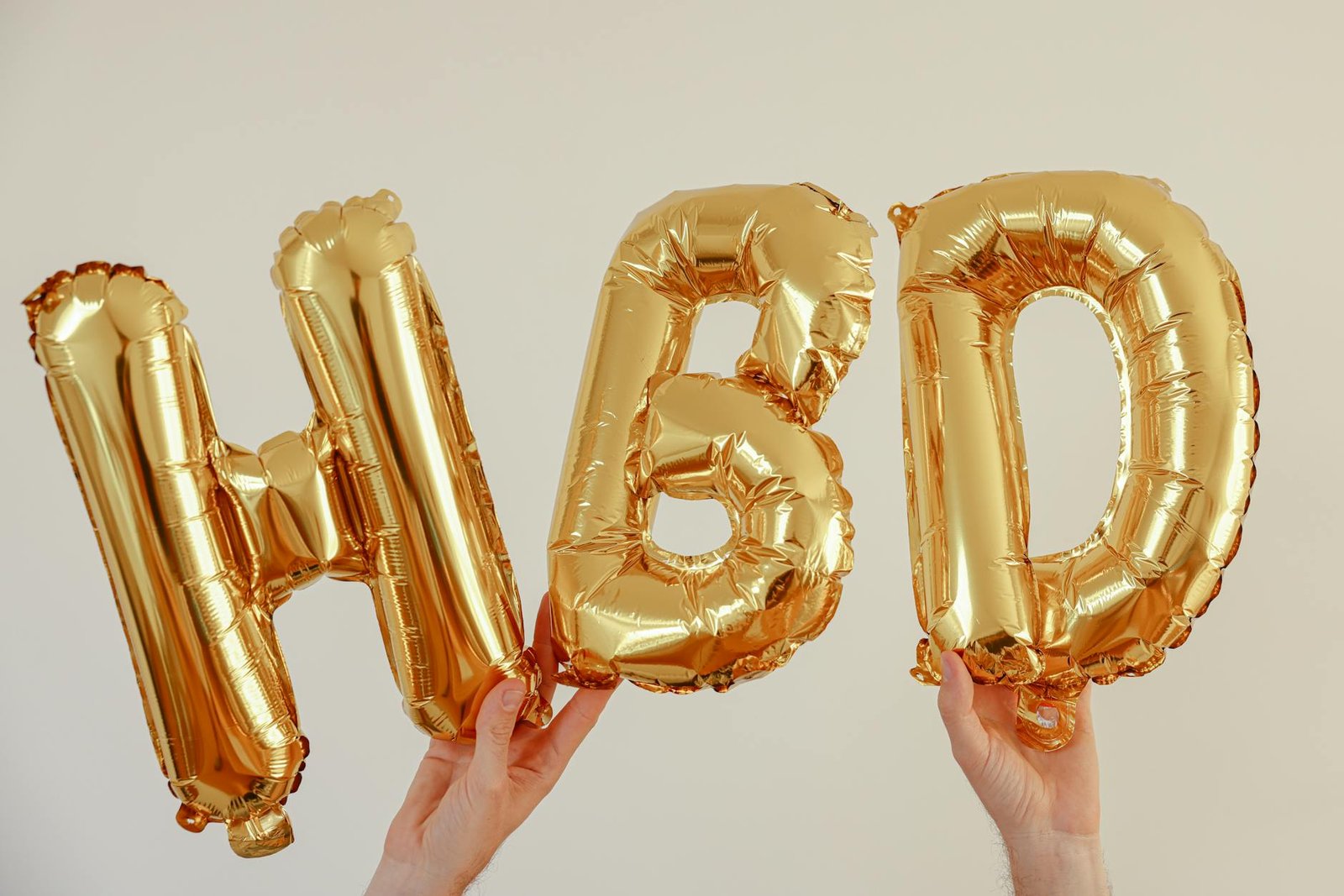 Gold balloon letters spelling HBD for Happy Birthday on a white background.